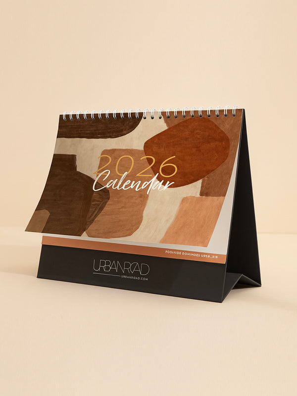 The Urban Road 2026 Desk Calendar by Urban Road AUS is a limited edition, spiral-bound calendar with abstract brown and beige shapes on the cover, standing on a black base featuring "URBAN ROAD" and "urbanroad.com" at the bottom.