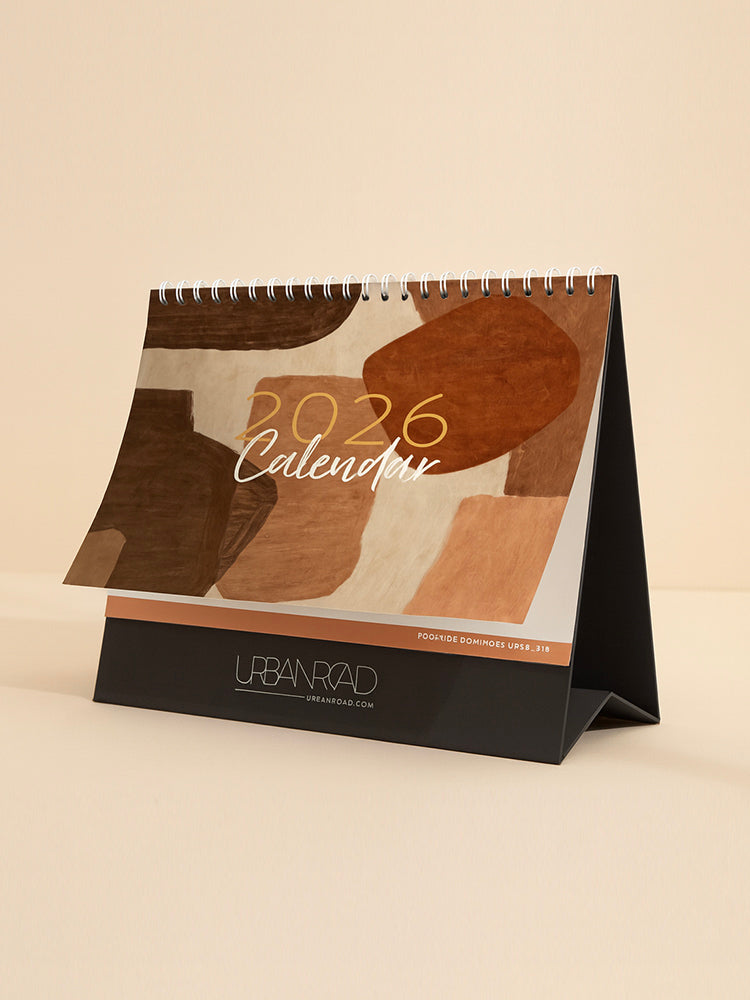 The Urban Road 2026 Desk Calendar by Urban Road AUS is a limited edition, spiral-bound calendar with abstract brown and beige shapes on the cover, standing on a black base featuring "URBAN ROAD" and "urbanroad.com" at the bottom.