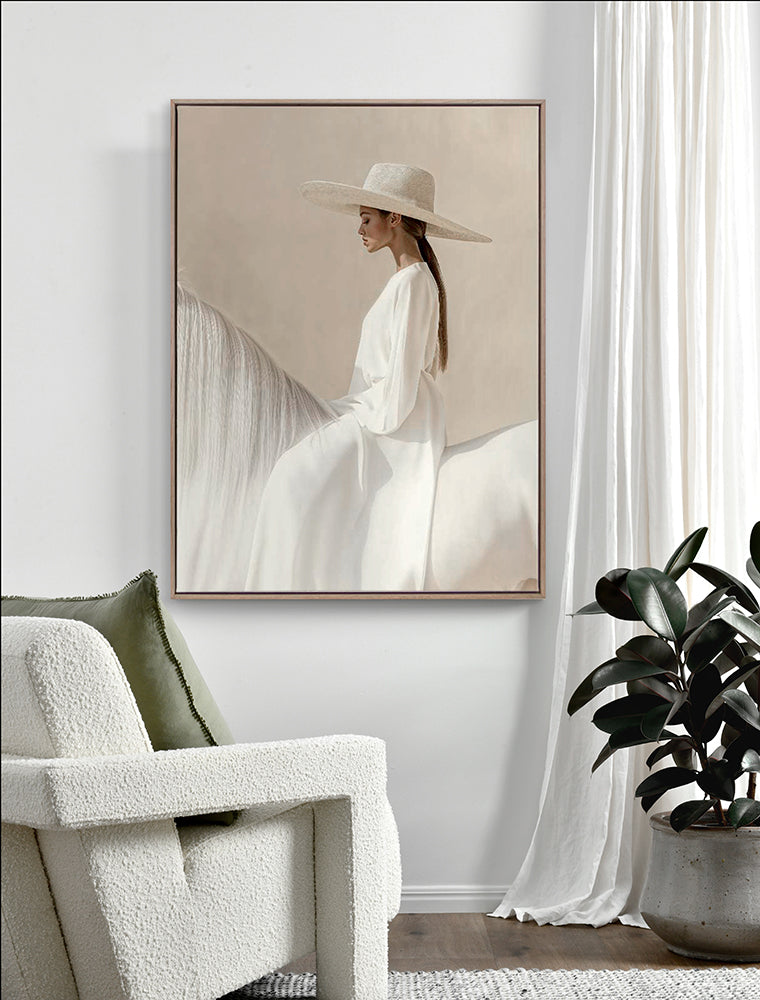 The "Texas Hold ‘Em - Oak Box Frame Canvas - 90x120 - Portrait" by Urban Road showcases equestrian art of a woman in a white dress and hat riding side-saddle, displayed above a white armchair beside a potted plant and white curtains.