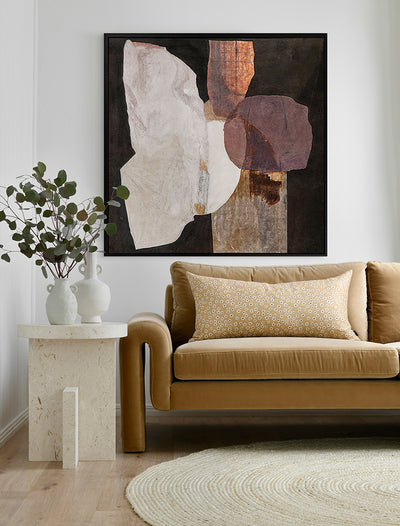 A modern living room with a tan sofa, patterned cushion, round beige rug, stone side table with two white vases of greenery, and Urban Road’s 'Chiaroscuro II' (90x90, Black Box Frame Canvas) wall art displayed above.