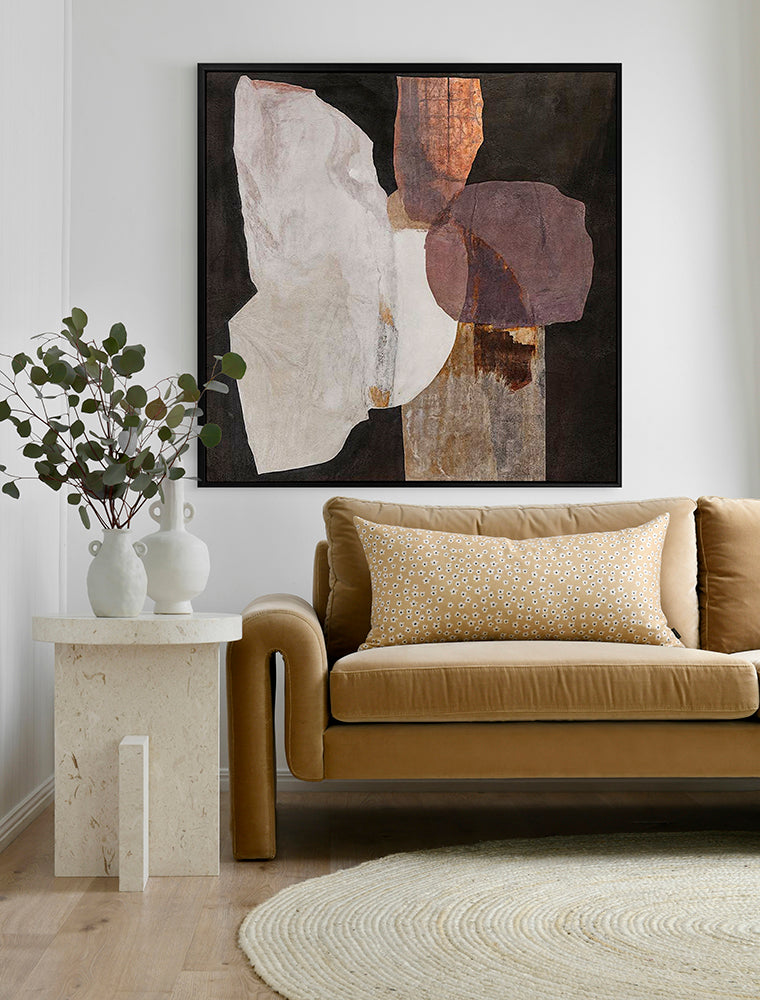 A modern living room with a tan sofa, patterned cushion, round beige rug, stone side table with two white vases of greenery, and Urban Road’s 'Chiaroscuro II' (90x90, Black Box Frame Canvas) wall art displayed above.