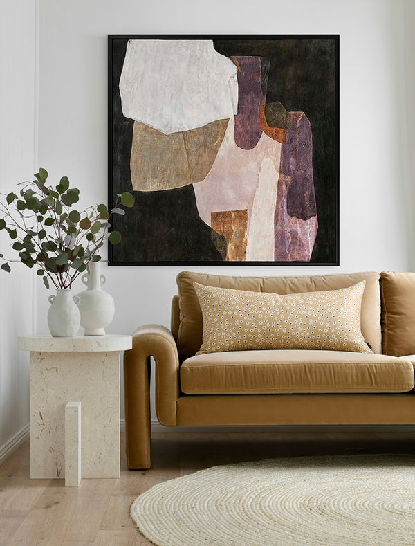 A modern living room with a tan sofa, patterned yellow cushion, round rug, stone side table with vases and branches, and Urban Road’s Chiaroscuro I - Black Box Frame Canvas (90x90) as striking square wall art above the sofa.