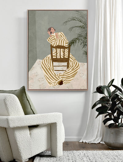 A modern living room features a white textured armchair, green cushion, potted plant, and the "Thessy" Oak Box Frame Canvas (90x120, Portrait) by Urban Road—artwork of a striped figure beside a chair and tall plant on a muted background.