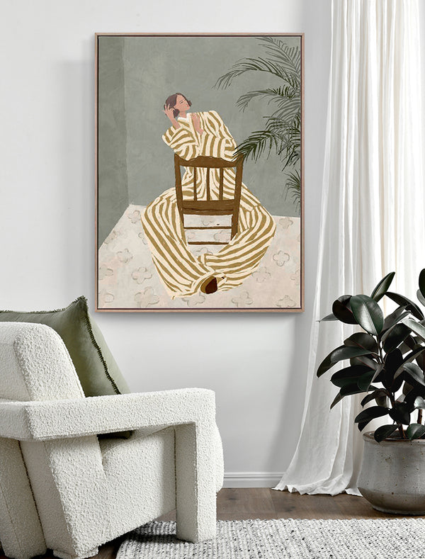A modern living room features a white textured armchair, green cushion, potted plant, and the "Thessy" Oak Box Frame Canvas (90x120, Portrait) by Urban Road—artwork of a striped figure beside a chair and tall plant on a muted background.