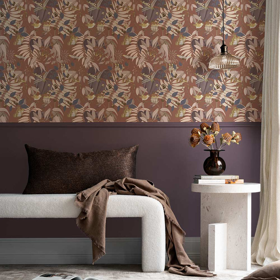 A cozy corner with a dark gray armchair, patterned pillow, marble side table with yellow flowers, and a pendant light. The wall features Urban Road’s Tales of the Bushland Buddies Wallpaper with green tropical leaves above a deep green panel.
