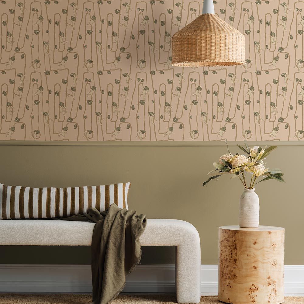 A young girl sits on a rug in a modern living room with a fluffy dog, plush toys, and cushions, all set against the Urban Road Giggly Bush Babies Wallpaper in soft olive green, adding a playful touch to the space.
