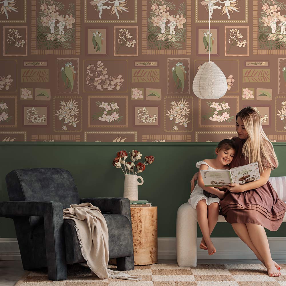 A young child smiles on a beige rug, hugging a teddy bear in a cozy living room featuring Urban Road's Little Bushland Memories Wallpaper, modern white chairs, a wooden side table, and a vase of flowers.
