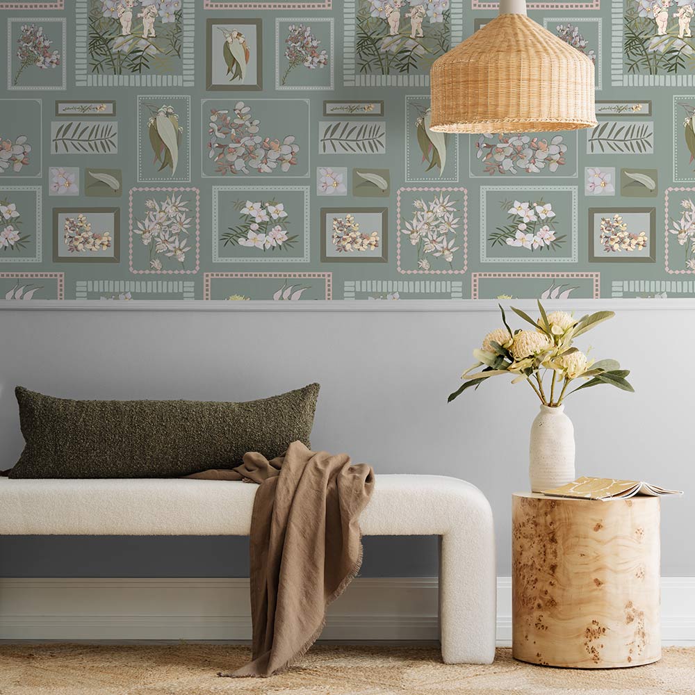 A young child smiles on a beige rug, hugging a teddy bear in a cozy living room featuring Urban Road's Little Bushland Memories Wallpaper, modern white chairs, a wooden side table, and a vase of flowers.
