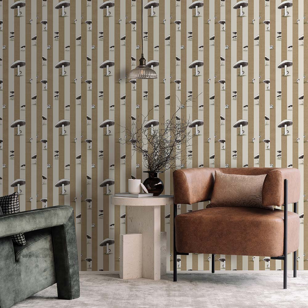 A cozy pink armchair with a cushion sits by a wooden side table and dried flowers, against a wall adorned with Urban Road’s Toadstool Peakaboo Dark Wallpaper, beneath a woven pendant light.
