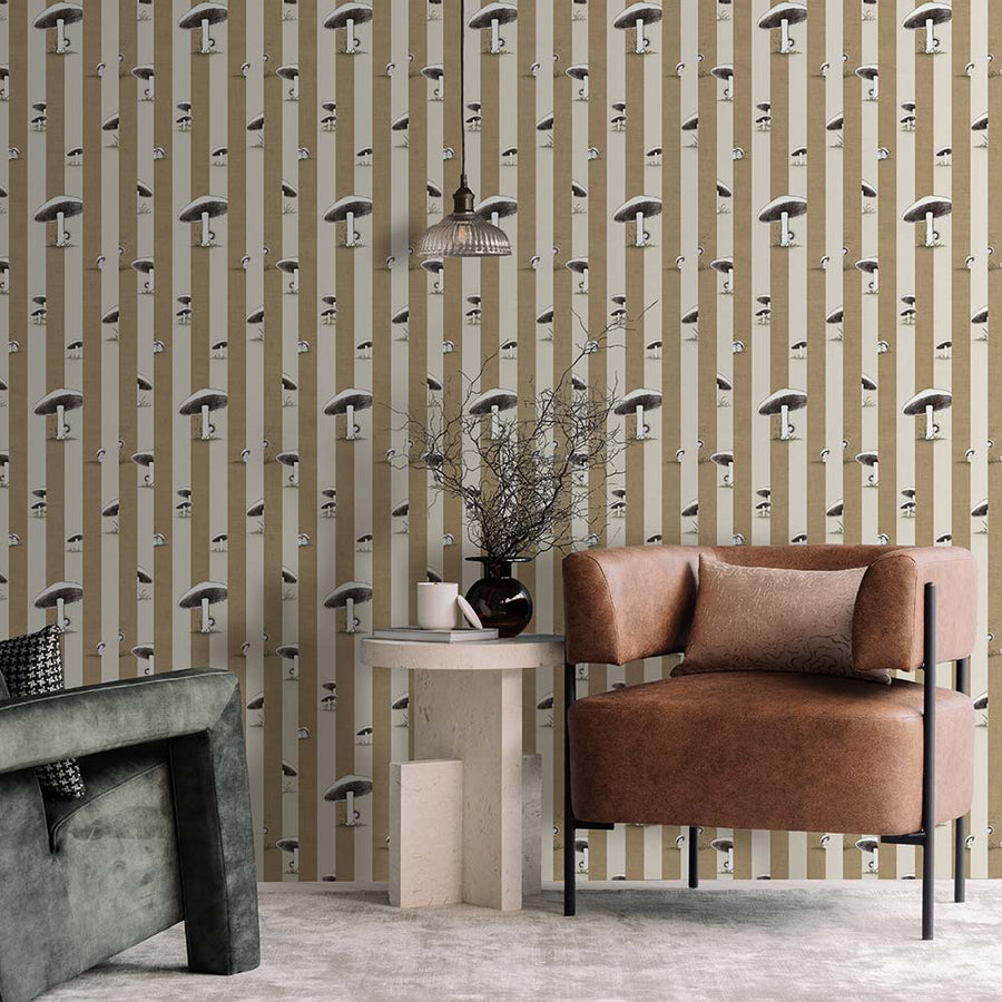 A cozy pink armchair with a cushion sits by a wooden side table and dried flowers, against a wall adorned with Urban Road’s Toadstool Peakaboo Dark Wallpaper, beneath a woven pendant light.
