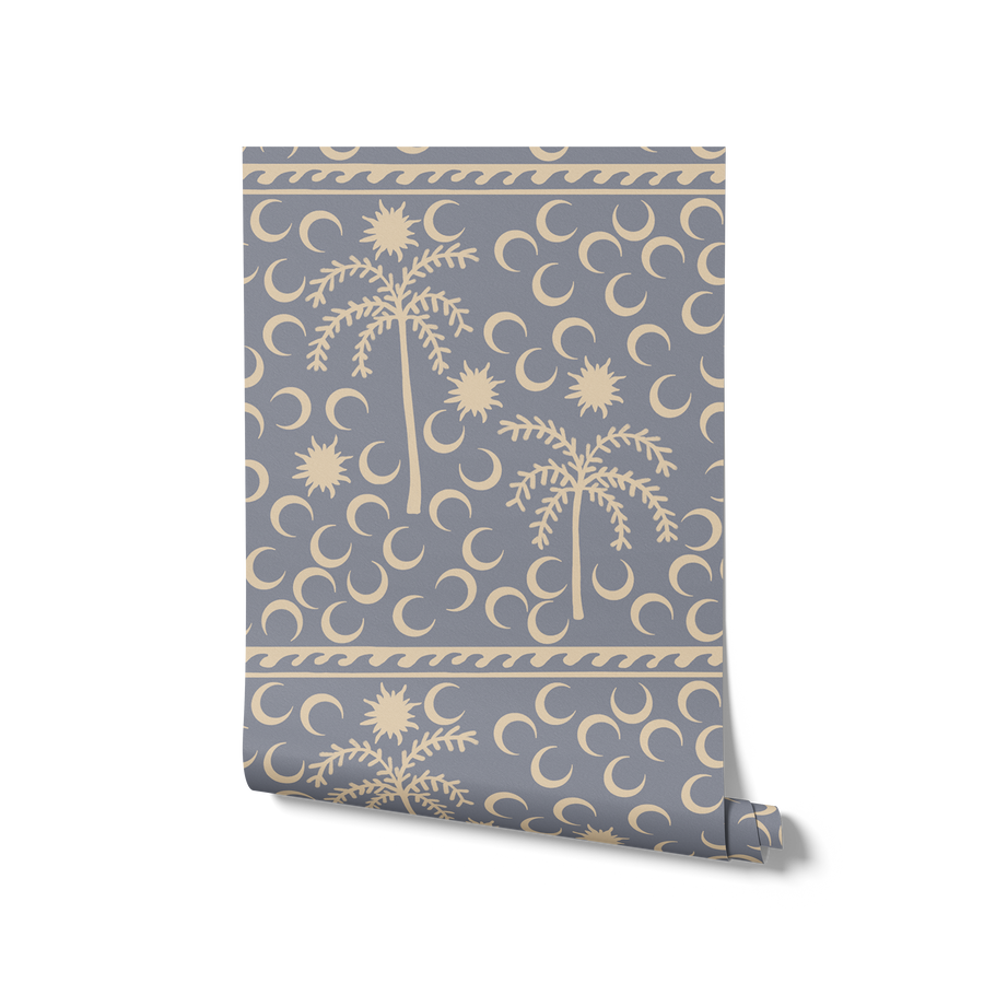 Dusty blue wallpaper with warm cream palm trees, moons, and a decorative woven-style header, from the Shatha collection with Urban Road.