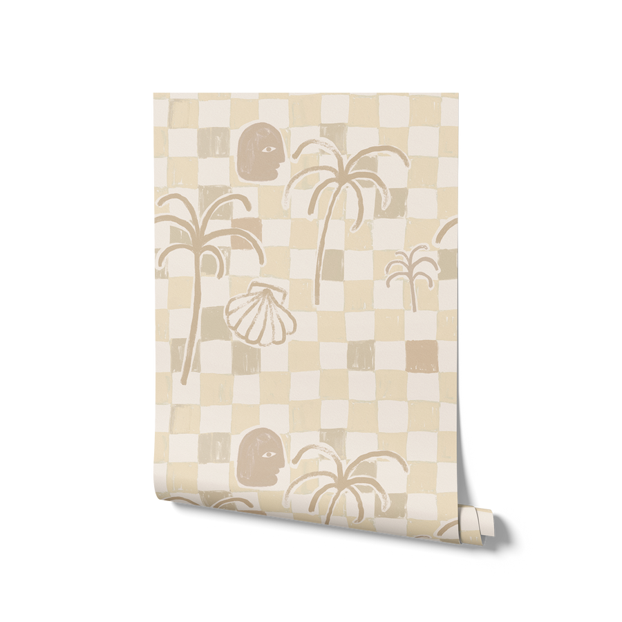 Neutral-toned wallpaper in sandy beige with a loose checker pattern, simple palm forms, and illustrated shell and face motifs, from the Shatha collection with Urban Road.