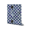 Deep blue checkered wallpaper with cream and cobalt elements, layered with palms, shells, and an illustrated black face profile, from the Shatha collection with Urban Road.