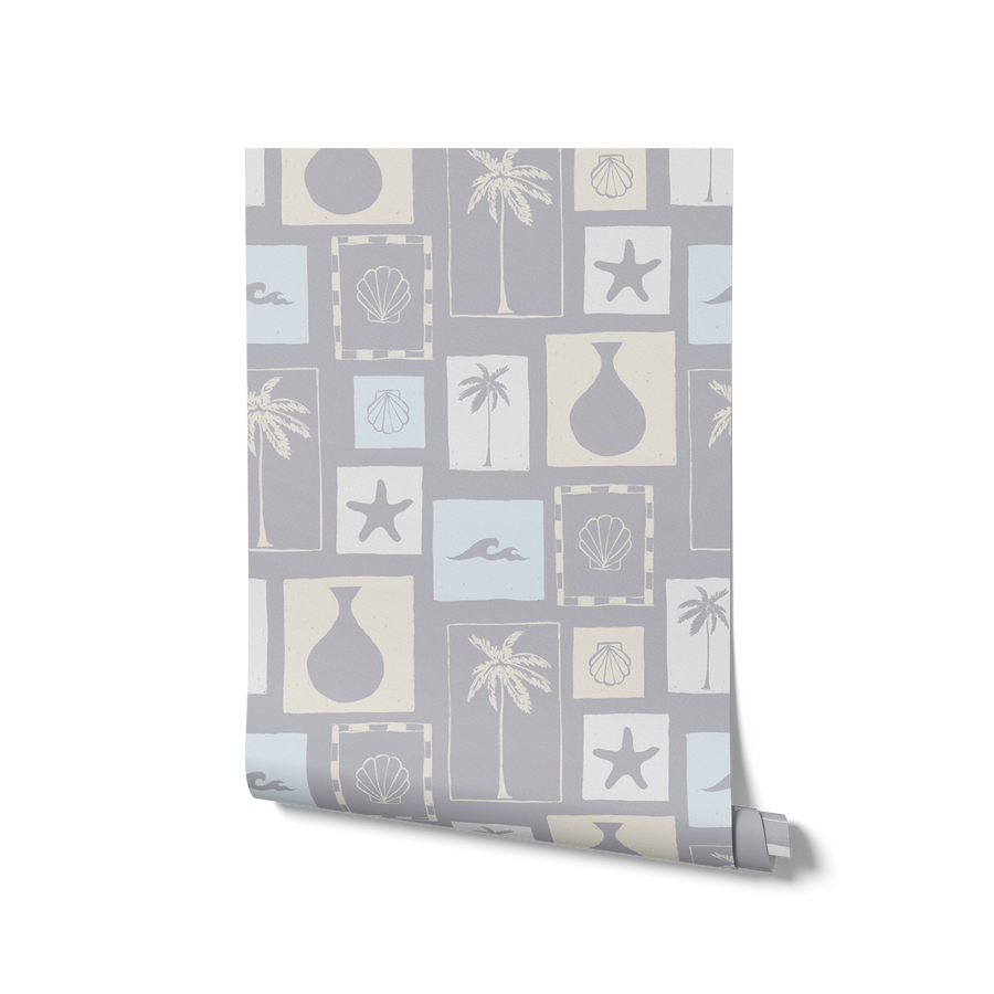 Light blue wallpaper with soft cream coastal illustrations in a patchwork of framed motifs including palms, seashells, and waves, from the Shatha collection with Urban Road.