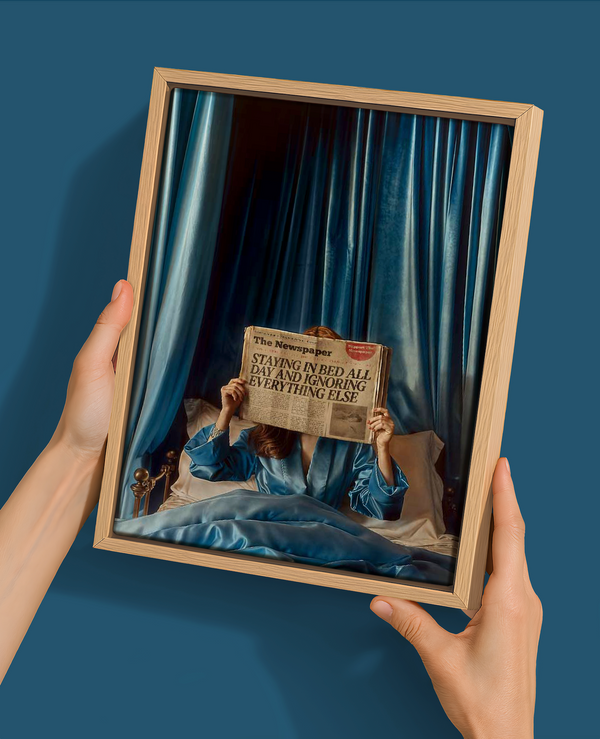 A person in blue pajamas sits on a blue-sheeted bed holding a newspaper that reads "STAYING IN BED ALL DAY AND IGNORING EVERYTHING ELSE" in Urban Road's Morning Gossip, a 22.5x30 oak box frame canvasâ€”perfect as mid-century modern wall art.