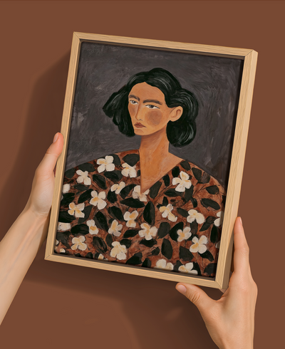 A person holds the "Céline - Oak Box Frame Canvas - 22.5x30 - Portrait" by Urban Road, featuring a woman with short dark hair, a serious expression, and a floral-patterned garment against a muted dark background.