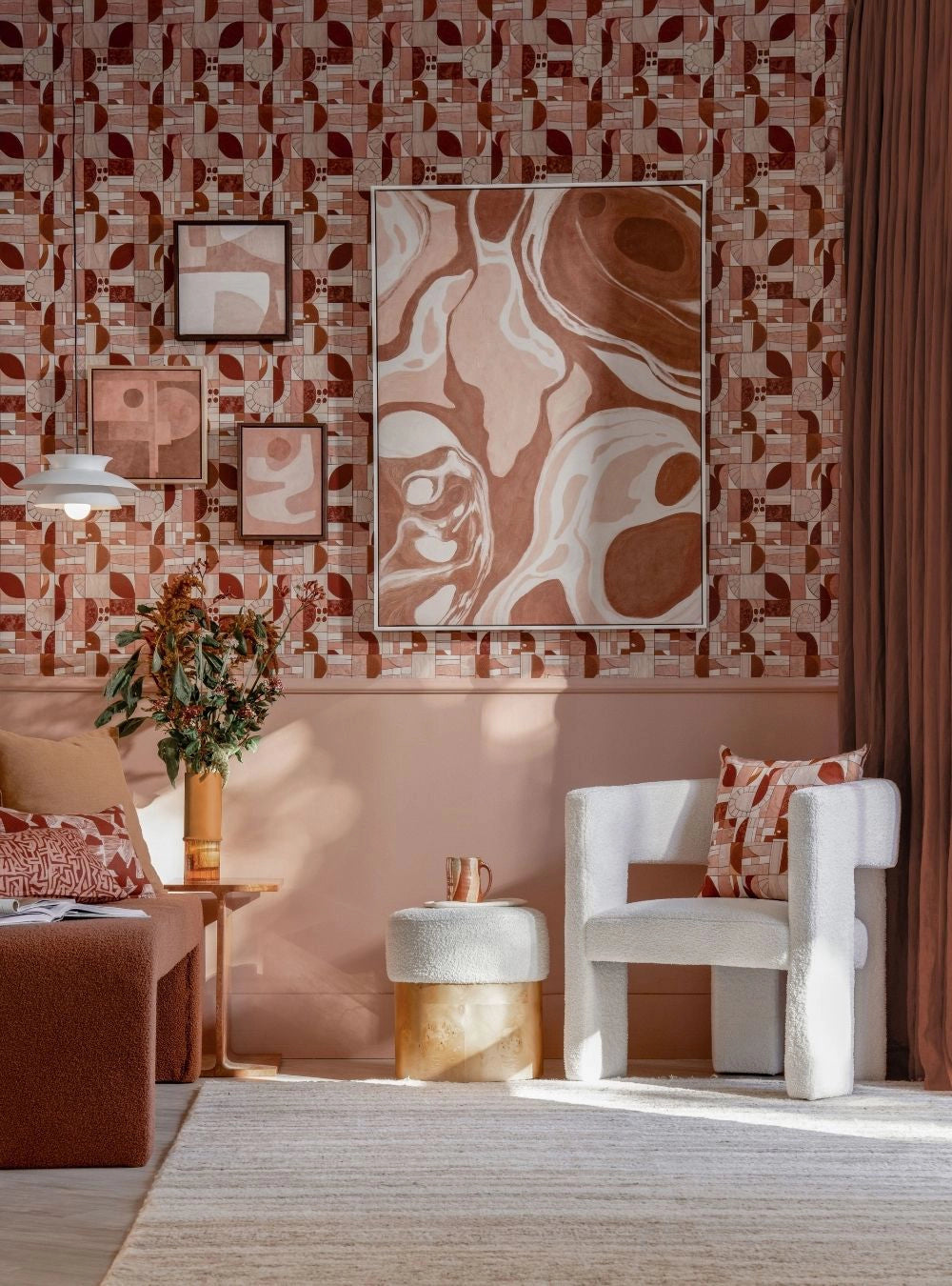 A cozy room with pink geometric wallpaper, abstract art, white boucle chair, and red-toned decor accents.