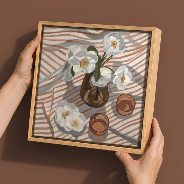 A pair of hands holds Urban Road's "Never a Fleeting Moment" wall art, a 30x30 Oak Box Frame Canvas featuring a still life with a vase and white flowers against a brown and gray striped background.