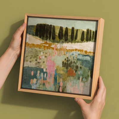 Two hands hold the Urban Road "Finding Your Way III" canvas (30x30, Oak Box Frame), featuring an abstract landscape with vertical tree forms and soft green, pink, and blue tones on a muted olive background.