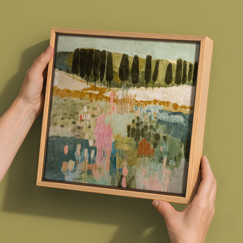 Two hands hold the Urban Road "Finding Your Way III" canvas (30x30, Oak Box Frame), featuring an abstract landscape with vertical tree forms and soft green, pink, and blue tones on a muted olive background.