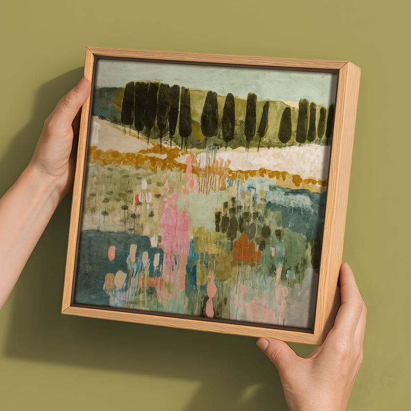 Two hands hold the Urban Road "Finding Your Way III" canvas (30x30, Oak Box Frame), featuring an abstract landscape with vertical tree forms and soft green, pink, and blue tones on a muted olive background.