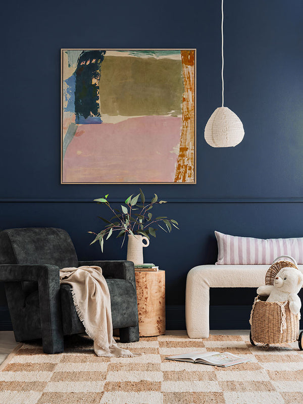 Desert Blush I abstract wall art print against a dark blue wall styled with seating furniture, decor and a checkered rug.