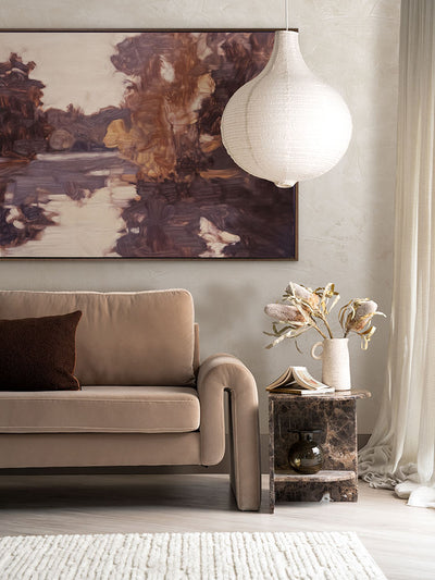 Sunset at Lavender Lake II landscape artwork above a beige velvet sofa with neutral decor and a pendant light in the corner.