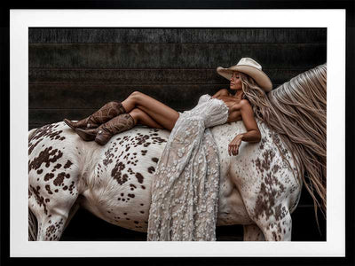 Glamorous photographic horse wall art featuring a woman in a cowboy hat and boots relaxing on a horse in earthy tones.