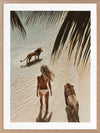 Photographic wall art of a woman and lions walking on a tropical beach with palm leaves, depicting adventurous strength.