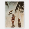 Photographic wall art of a woman and lions walking on a tropical beach with palm leaves, depicting adventurous strength.