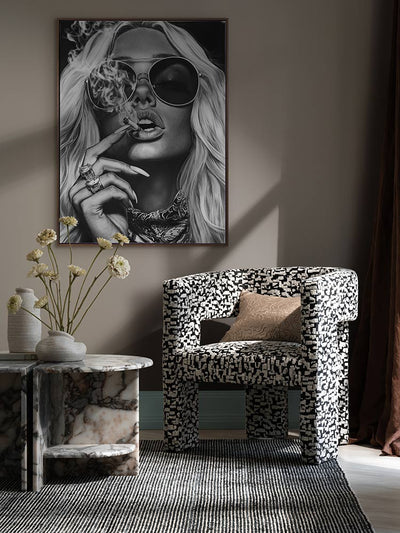 Femme Fatale portrait print styled above an armchair and marble side table with moody lighting and modern decor elements.