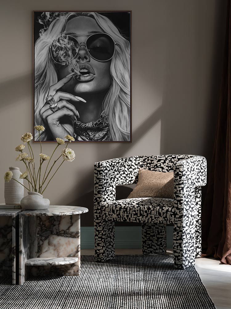 Femme Fatale portrait print styled above an armchair and marble side table with moody lighting and modern decor elements.