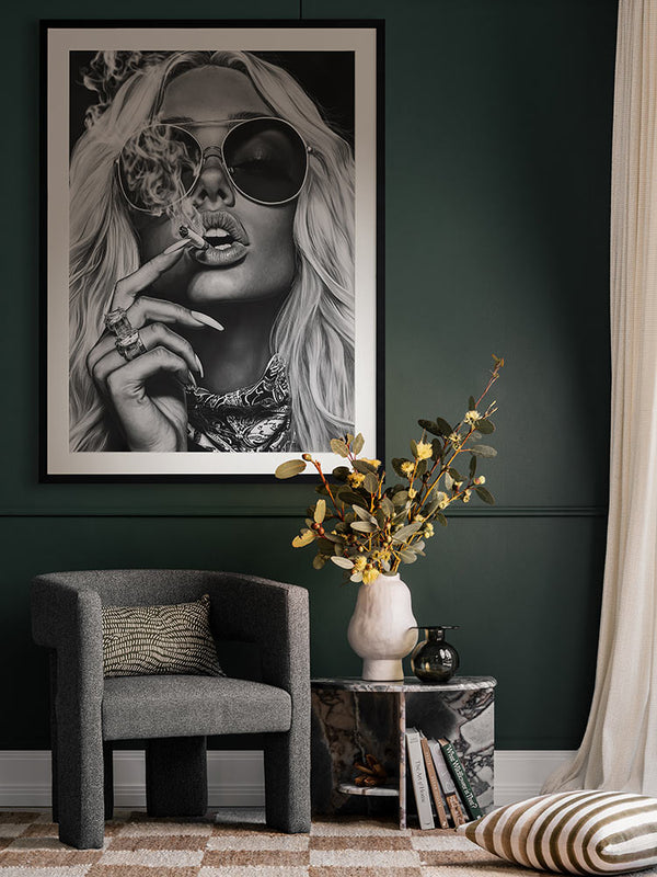 Femme Fatale portrait print styled above an armchair and marble side table with moody lighting and modern decor elements.