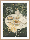 A soft garden scene with a white table set for tea among lush greenery, featuring pastries and striped linens. From the Lounging Ladies II collection by Urban Road.