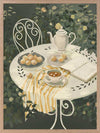 A soft garden scene with a white table set for tea among lush greenery, featuring pastries and striped linens. From the Lounging Ladies II collection by Urban Road.
