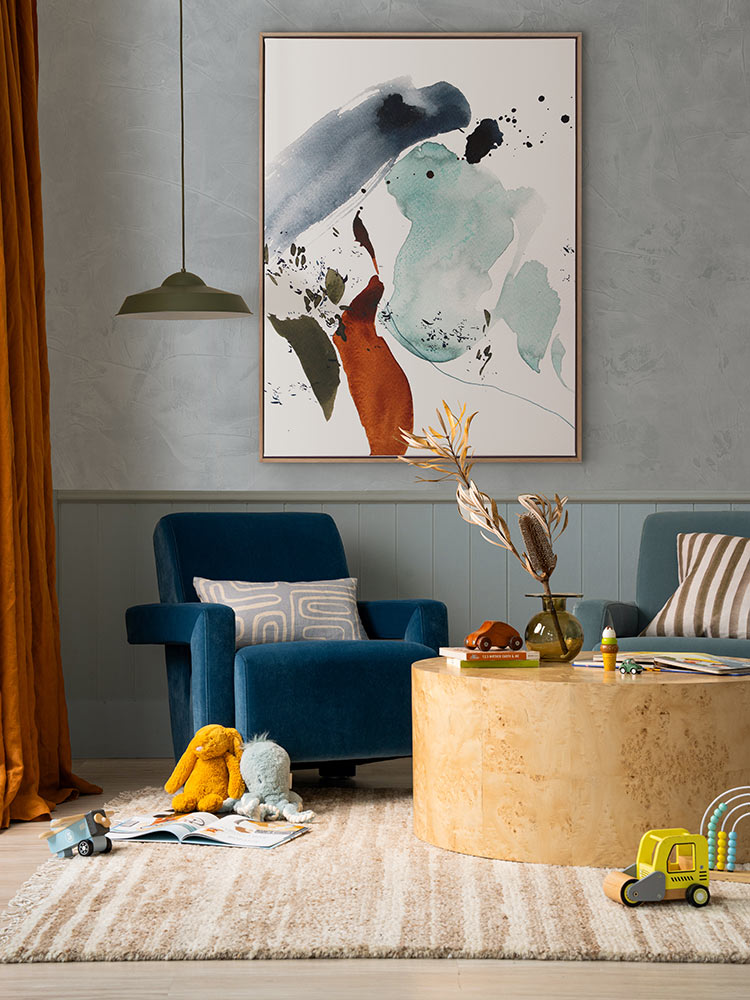 Rainwater abstract artwork hanging above blue and green armchairs, styled with neutral decor, orange curtains and kids toys.