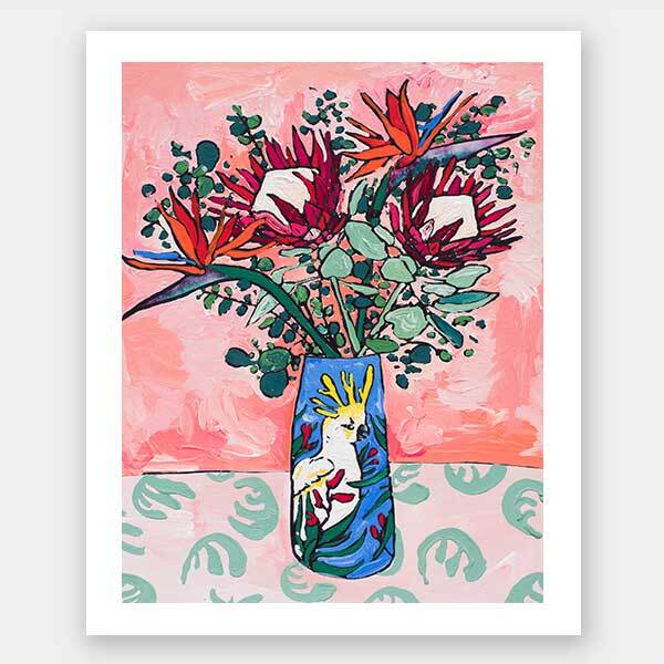 The "Pink Cockatoo Unframed Art Print" by Urban Road features colorful proteas and kangaroo paws in a floral vase set on a green patterned table, with a pink abstract background for vibrant still life decor.