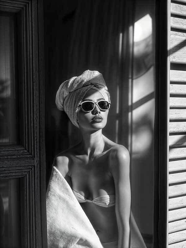 A woman in sunglasses and a towel wrap stands by a window in a bikini top. Dramatic light and shadows give Art Deco flair to this black-and-white photo, featured on the Morning Glow Canvas Art Print from Shaynna Blaze x Urban Road.