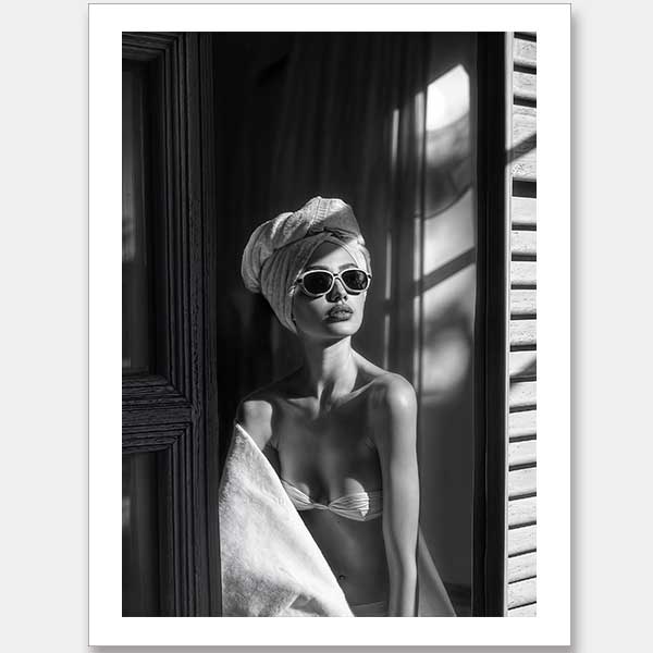 Morning Glow Unframed Art Print by Shaynna Blaze x Urban Road features a black and white image of a woman in sunglasses and towel by a sunlit window, evoking Art Deco wall art as she gazes thoughtfully in her bikini top.