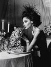 A woman in a chic black dress and feathered hat dines by candlelight with a cheetah in this glamorous, vintage-inspired scene—perfectly captured in the "Feline Couture Canvas Art Print" by Shaynna Blaze x Urban Road.