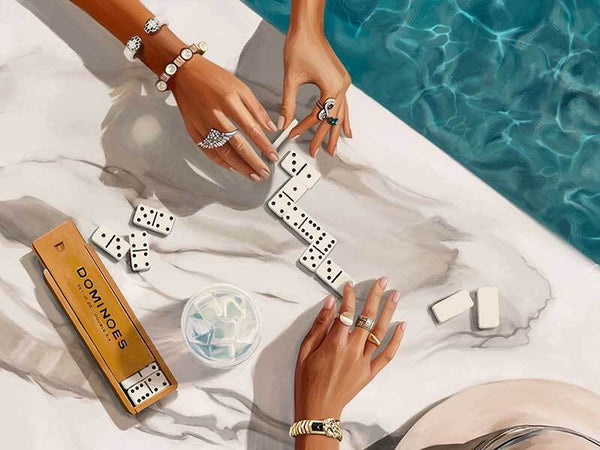 Two people with manicured hands and jewelry play dominoes poolside, with a marble table and sunlight—capturing the luxury of Shaynna Blaze x Urban Road’s Poolside Dominoes Canvas Art Print.