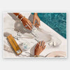 Two people with manicured hands and jewelry play dominoes on marble by a poolside, with a gold domino box and drink nearby in this sunlit scene—featured in the Poolside Dominoes Unframed Art Print by Shaynna Blaze x Urban Road.