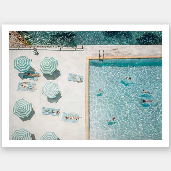 The Bondi Bathers Club Unframed Art Print by Shaynna Blaze x Urban Road features a sunlit aerial view of swimmers and sunbathers lounging under green-and-white striped umbrellas, evoking the charm of the vintage Bondi Bathers Club.