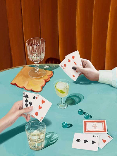 Two people play cards at a turquoise table with drinks and dice, set against orange curtains. The Deal Me In Canvas Art Print by Shaynna Blaze x Urban Road brings nostalgic, vintage flair to any space.