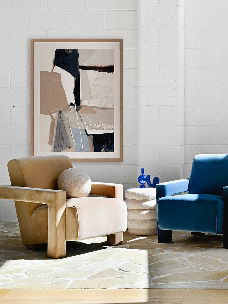 A framed Equilibrium I art print hanging in a modern living space. The artwork features bold brushstrokes in navy, beige, and white, styled with a textured armchairs and neutral decor.