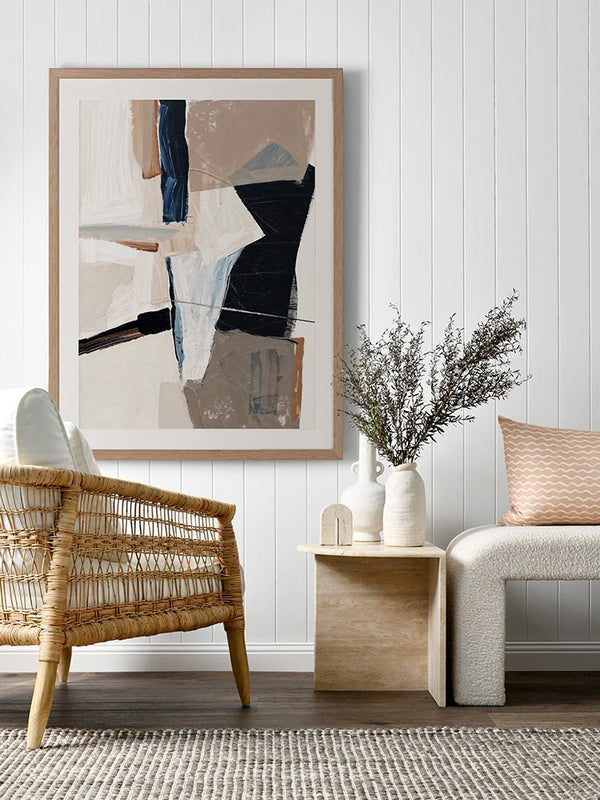 A framed Equilibrium III art print hanging in a bright, modern entryway. The artwork features bold navy, beige, and white brushstrokes, paired with a bench and woven decor accents.
