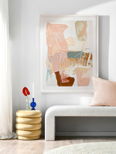 A framed Floating On Air I art print displayed in a lighter toned living space with a white bench, a soft white rug, flowy sheer curtains, and cosy decor.