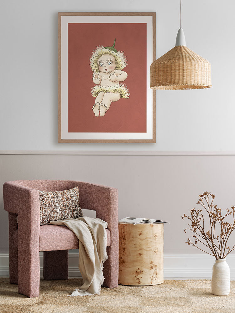 A cozy, modern room features a pink textured armchair, wooden side table, dried plant, and Urban Road’s Gum Blossom Baby III Terracotta Framed Art Print on a mauve wall. A woven pendant lamp hangs overhead.