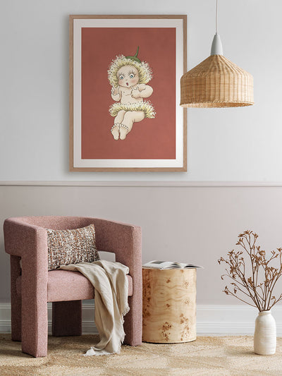 A cozy, modern room features a pink textured armchair, wooden side table, dried plant, and Urban Road’s Gum Blossom Baby III Terracotta Framed Art Print on a mauve wall. A woven pendant lamp hangs overhead.