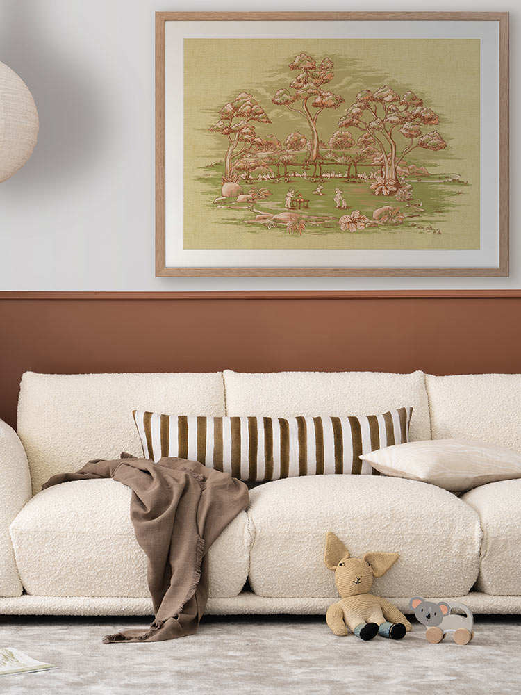 A cozy living room features a cream sofa with a striped pillow and throw, plush toys on the floor, and Urban Road’s The Gumnut Spring Parade Light Green Framed Art Print above the sofa, adding Australian bush charm.
